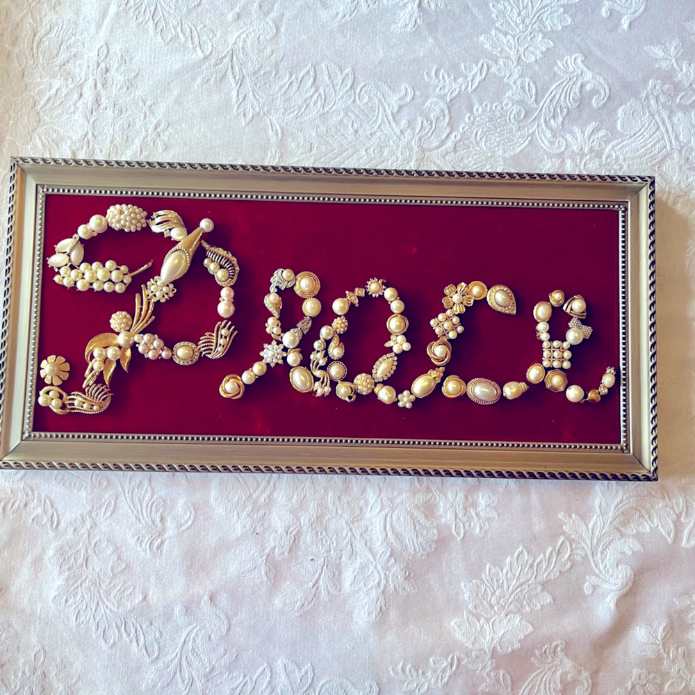 Peace/red velvet in a silver metal frame that sits on a table 15”L X 7”H